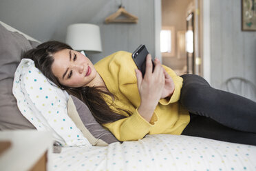 Frau benutzt Smartphone, während sie zu Hause auf dem Bett liegt - CAVF03578