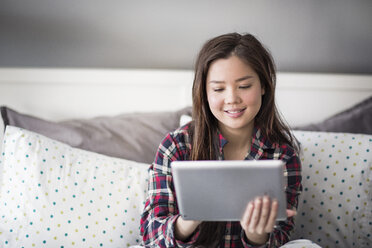 Frau benutzt Tablet-Computer, während sie zu Hause auf dem Bett sitzt - CAVF03583