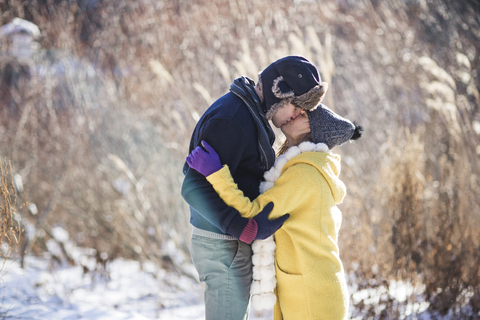 Seitenansicht eines Paares, das sich küsst, während es auf einem schneebedeckten Feld steht, lizenzfreies Stockfoto