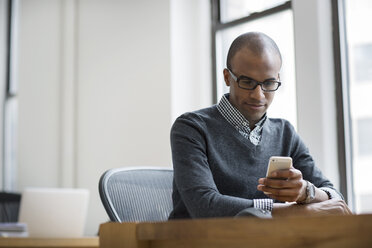 Businessman using smart phone while sitting by desk in office - CAVF03617