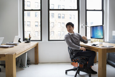 Businessman looking over shoulder while working in office - CAVF03620