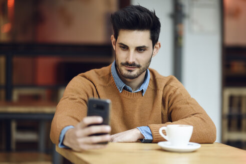 Porträt eines jungen Mannes, der in einem Café sitzt und ein Mobiltelefon benutzt - JSMF00103