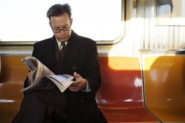 Geschäftsmann beim Lesen einer Zeitschrift während der Fahrt im Zug - CAVF03662