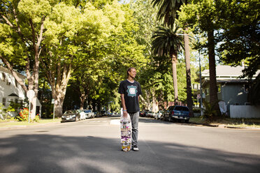 Mann hält Skateboard und steht auf der Straße - CAVF03680