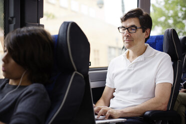 Mann, der im Bus sitzend einen Laptop benutzt - CAVF03706