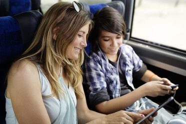 Mutter und Sohn schauen auf einen Tablet-Computer, während sie im Bus sitzen - CAVF03709