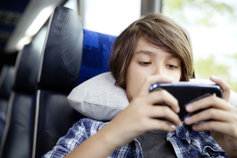 Nahaufnahme eines Jungen, der ein Mobiltelefon benutzt, während er im Bus sitzt, lizenzfreies Stockfoto