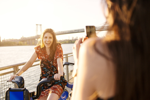 Frau fotografiert Freund auf Fahrrad gegen klaren Himmel, lizenzfreies Stockfoto