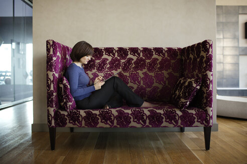 Geschäftsfrau, die einen Tablet-Computer benutzt, während sie auf dem Sofa im Büro sitzt - CAVF03830