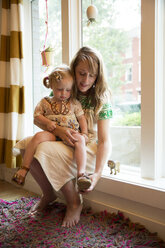 Mother assisting daughter in wearing shoes while sitting at window in home - CAVF03849