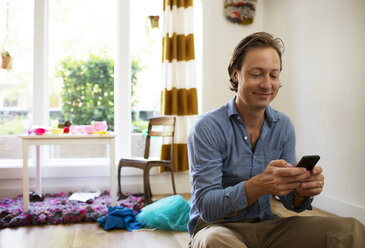 Happy man using mobile phone at home - CAVF03860