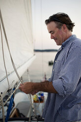 Side view of happy man tying rope while standing at yacht - CAVF03955