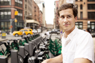 Man looking away while standing at bicycle parking station in city - CAVF03965