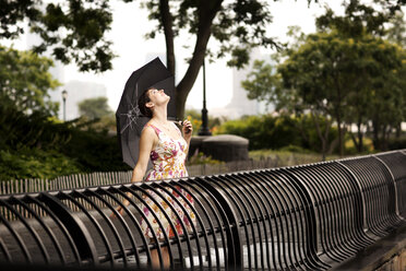 Carefree woman with umbrella looking up while standing by railing - CAVF03991