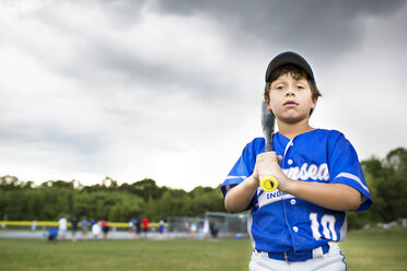Porträt eines Jungen mit Baseballschläger auf einem Feld vor bewölktem Himmel - CAVF04073