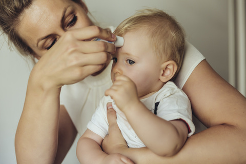 Die Mutter misst die Temperatur des Babys mit einem Hautthermometer, lizenzfreies Stockfoto