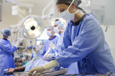 Nurse wearing scrubs preparing medical instruments in operating theater - CAIF08450