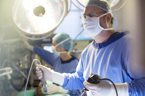 Männlicher Chirurg hält Laparoskopie-Ausrüstung während einer Operation im Operationssaal - CAIF08456