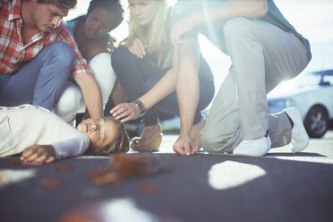 Friends examining injured girl on sidewalk - CAIF08516