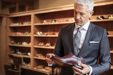 Businessman shopping for dress shoes in menswear shop - CAIF08556