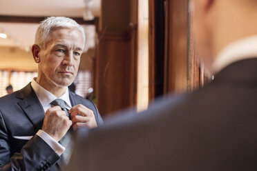 Businessman trying on tie in mirror in menswear shop - CAIF08557