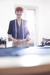 Porträt einer selbstbewussten Schneiderin, die eine Schere in einer Werkstatt für Herrenbekleidung hält - CAIF08568