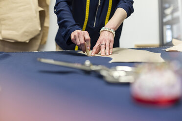 Female tailor marking fabric with pattern in menswear workshop - CAIF08569