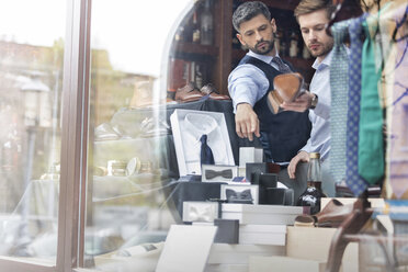 Arbeiter zeigt Geschäftsmann Ware im Schaufenster eines Herrenbekleidungsgeschäfts - CAIF08571