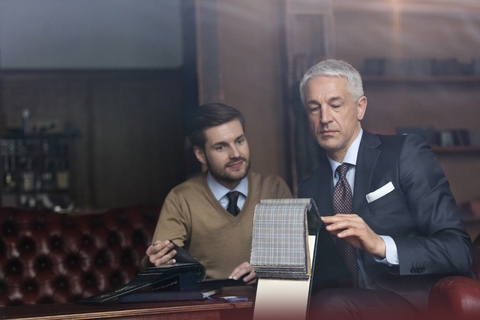 Schneider und Geschäftsmann beim Durchstöbern von Stoffen in einem Herrenbekleidungsgeschäft, lizenzfreies Stockfoto