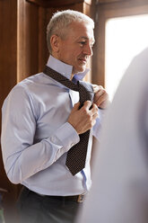 Geschäftsmann beim Anprobieren einer Krawatte in einem Herrenbekleidungsgeschäft - CAIF08584