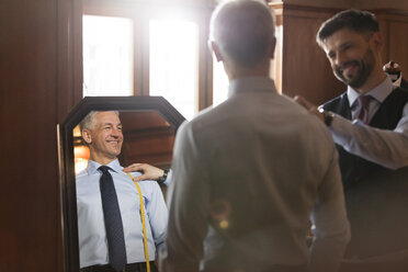 Tailor fitting businessman at mirror in menswear shop - CAIF08606