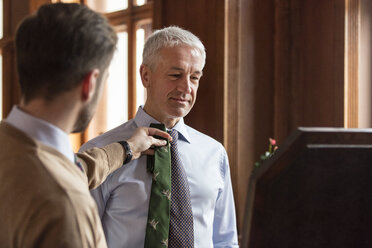Schneider zeigt Geschäftsmann Krawatten am Spiegel im Herrenbekleidungsgeschäft - CAIF08609