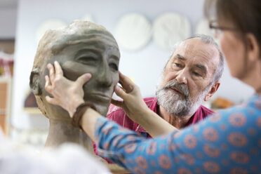 Woman sculpting clay face in pottery studio - CAIF08622