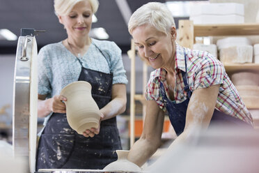 Ältere Frau hält Töpferware am Brennofen im Atelier - CAIF08625