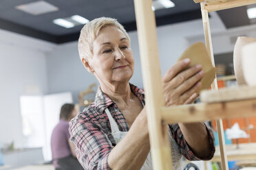 Lächelnde ältere Frau, die Töpferwaren auf ein Regal im Atelier stellt - CAIF08639