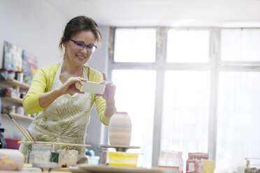 Ältere Frau fotografiert Keramikvase mit Fotohandy im Studio - CAIF08664