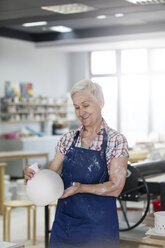 Smiling senior woman holding pottery vase in studio - CAIF08678