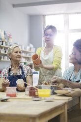 Lehrerin führt erwachsene Schüler beim Töpfern im Atelier an - CAIF08683