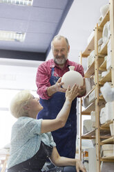 Lächelndes Paar stellt Keramikvase auf Regal in Atelier - CAIF08688