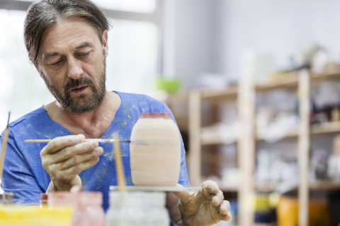 Konzentrierter reifer Mann beim Bemalen einer Keramikvase im Atelier, lizenzfreies Stockfoto