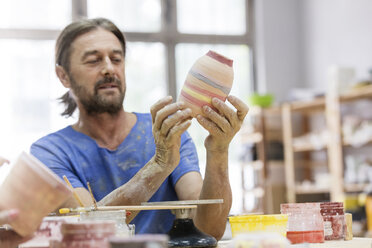 Älterer Mann bemalt Keramikvase im Atelier - CAIF08707