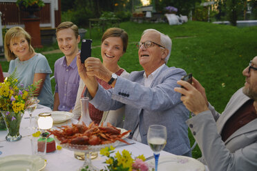 Älterer Mann, der ein Selfie mit seiner Familie beim Abendessen im Sommergarten macht - CAIF08717