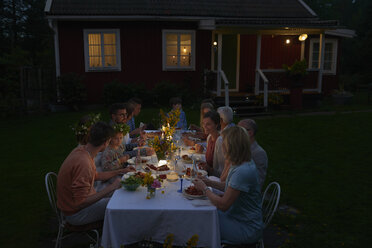 Familie genießt Abendessen bei Kerzenlicht am Terrassentisch vor dem Haus bei Nacht - CAIF08718