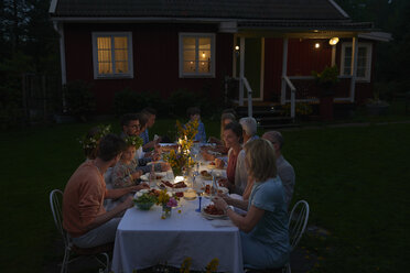 Family enjoying candlelight dinner at patio table outside house at night - CAIF08718