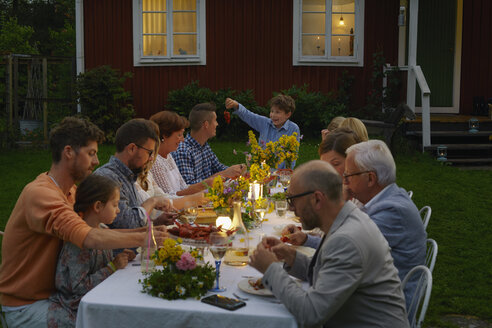 Familie genießt Abendessen bei Kerzenlicht im Garten - CAIF08720