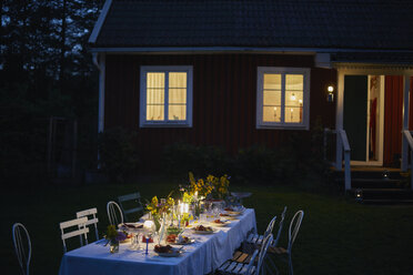 Gartenparty bei Kerzenlicht und Abendessen vor dem beleuchteten Haus bei Nacht - CAIF08721