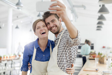 Enthusiastic couple taking selfie with camera phone in cooking class kitchen - CAIF08726