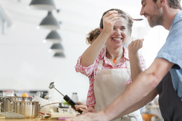Lächelndes Paar bei der Verkostung von Speisen in der Küche eines Kochkurses - CAIF08739