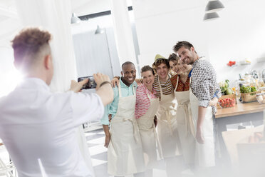 Chef teacher photographing students with camera phone in cooking class kitchen - CAIF08743