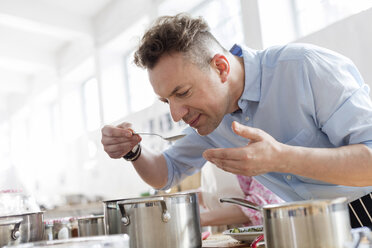 Man smelling food leaning over pot in cooking class kitchen - CAIF08751